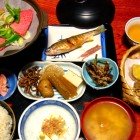 A typical dinner at a ryokan in Takayama includes kaiseki dishes with sashimi, sukiyaki, tempura, pickles, rice, and grilled fish, accompanied by local sake, in a serene and refined setting.